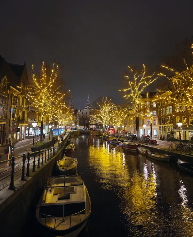 An Amsterdam canal at night, with trees strung with lights reflected in the water