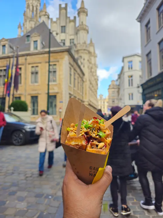 A waffle cone piled with toppings, held up on a Brussels street