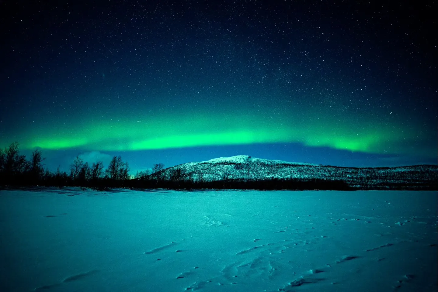 Green northern lights over snowy hills in Finland