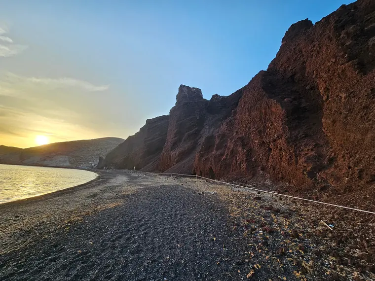 The red cliffs and dark pebbles of Red Beach, Santorini, in late light