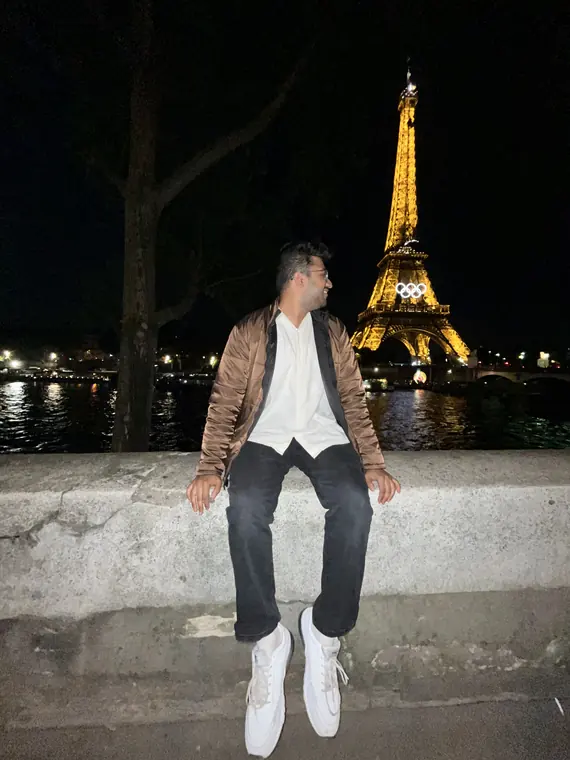 Sandeep sitting on a stone wall at night, with the lit-up Eiffel Tower behind him