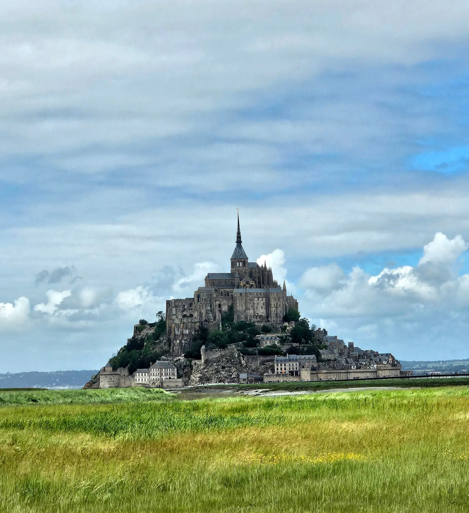 Mont Saint-Michel rising above green fields under a cloudy sky
