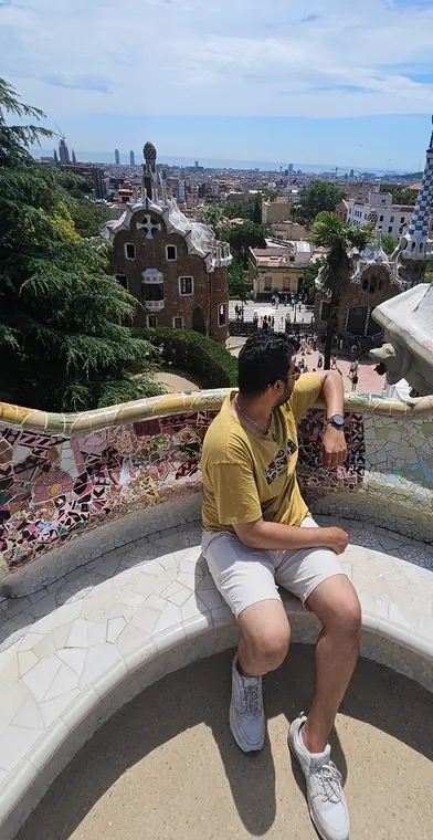 Sandeep sitting on the curved mosaic bench at Park Güell in Barcelona