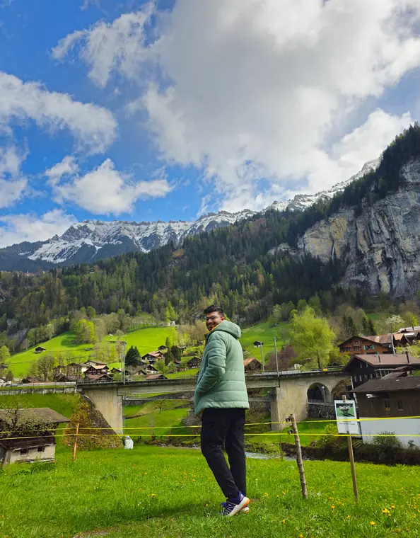 Sandeep standing in a green meadow in Lauterbrunnen, with cliffs and snowy peaks behind