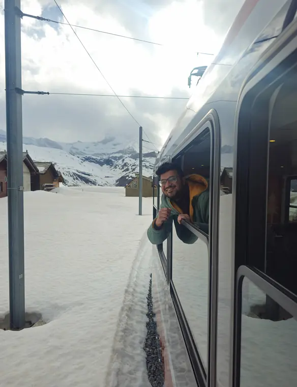 Sandeep leaning out of a train window, with snow beside the tracks