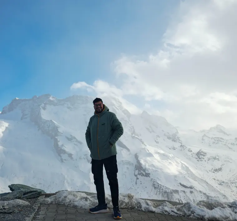 Sandeep standing on a snowy ridge above Zermatt, with glaciers and peaks behind