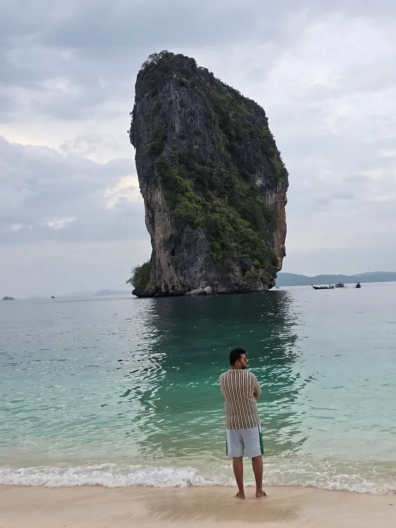 Sandeep standing in clear water at Koh Poda, with a limestone rock rising from the sea