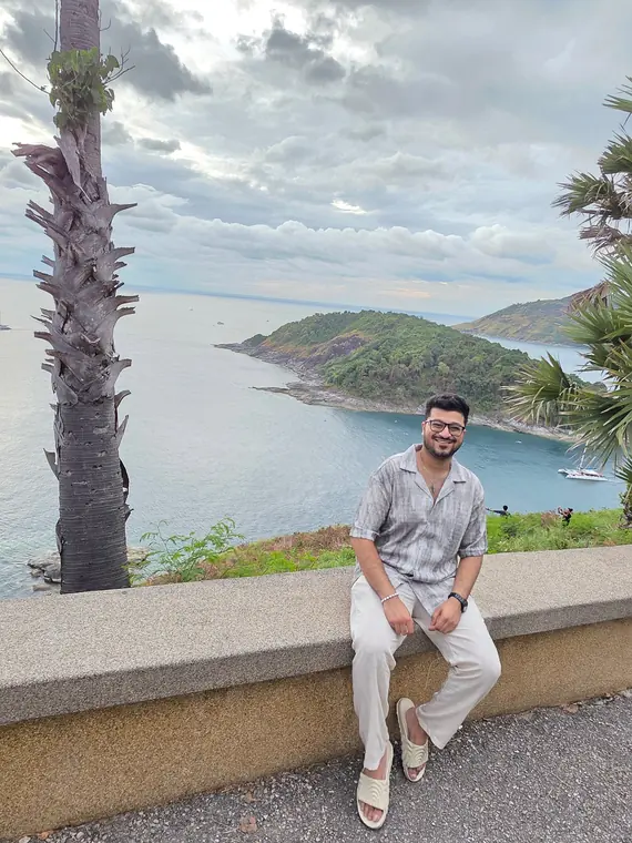 Sandeep sitting on a wall at a Phuket viewpoint, above the sea and islands