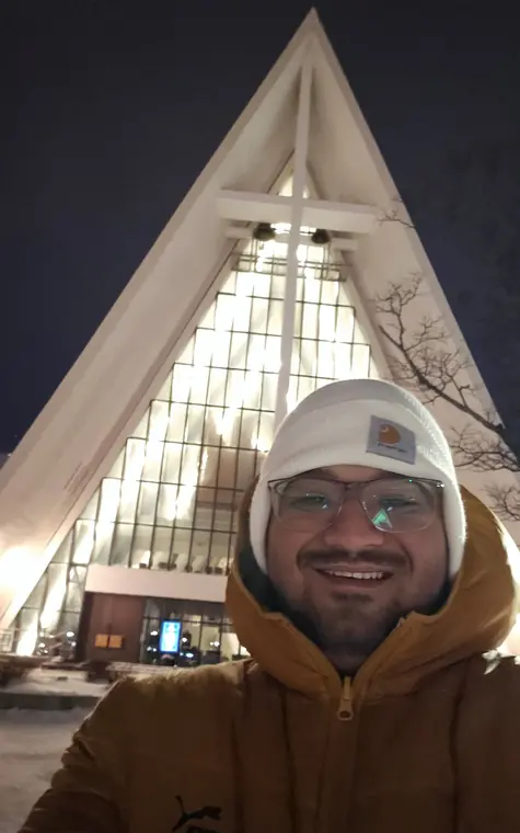 Sandeep in a winter hat taking a selfie in front of the lit-up Arctic Cathedral